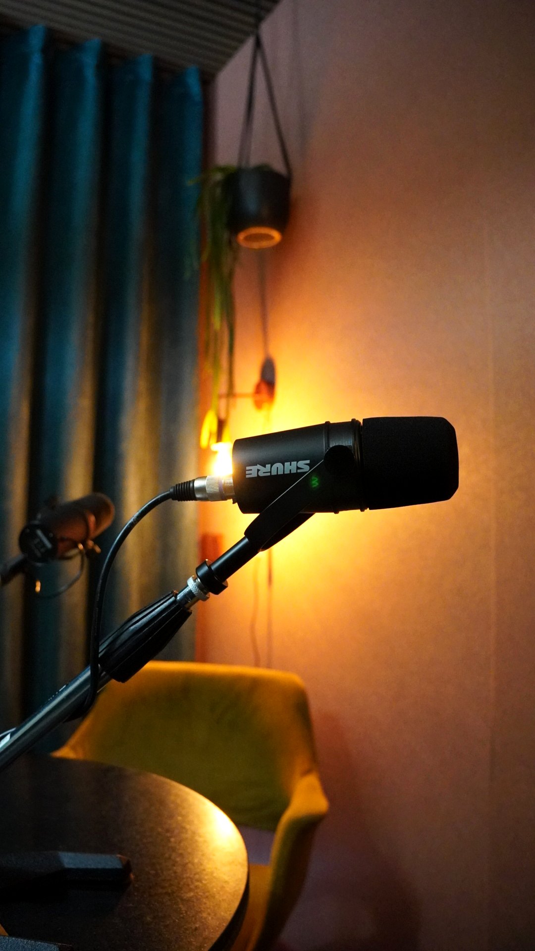 Shure-microfoon aan een arm in de studio, met warm licht en een okergele stoel